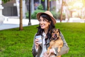 mulher jovem e bonita brincando com seu cachorro em um parque ao ar livre. retrato de estilo de vida. mulher hipster feliz brincando com seu cachorro e bebendo café. amor entre dono e cachorro. foto