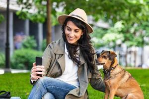 retrato de garota satisfeita abraçando cachorro engraçado e tirando uma selfie com seu celular. mulher jovem sorridente na camisa branca, aproveitando o bom dia e posando com animal de estimação foto