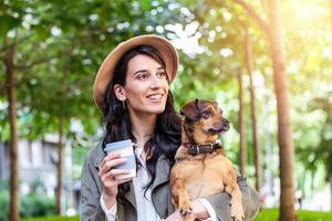 mulher hipster feliz brincando com seu cachorro e bebendo café. menina estilosa com cachorro engraçado descansando, abraçando e se divertindo no sol, momentos fofos. espaço para texto foto