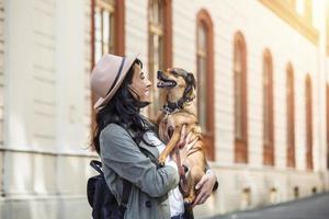 mulher hipster feliz brincando com seu cachorro na rua. menina estilosa com cachorro engraçado descansando, abraçando e se divertindo, momentos fofos. foto