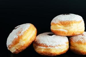 açúcar em pó é derramado em rosquinhas. tradicional sobremesa judaica sufganiyot em fundo preto. cozinhar berlinenses fritos. foto