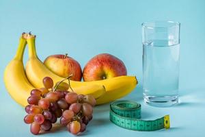 fruta, copo de água e fita métrica sobre um fundo azul. o conceito de dieta e nutrição adequada. foto