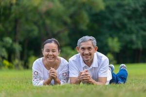 retrato de casal asiático sênior deitado na grama no parque público olhando para a câmera com boa saúde mental para longevidade e conceito de casamento feliz foto