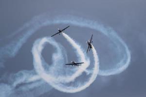 três aviões fazendo acrobacias em um show aéreo, com eles soltando fumaça