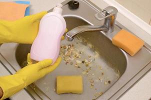 limpador mostra garrafa de detergente líquido de limpeza na pia da cozinha suja com partículas de alimentos antes da limpeza foto