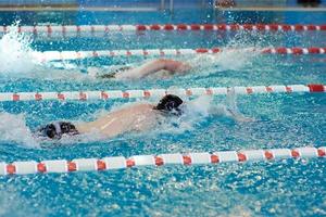 um nadador gorro estica os braços durante um treino de bruços na piscina, foco turvo foto