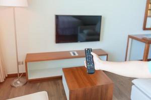 mão usando o controle remoto para ajustar a smart tv dentro do quarto moderno em casa. conceito de vida em apartamento foto