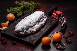 Stollen de torta de natal com maçapão, frutas e nozes em um fundo escuro de concreto foto