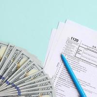 1120 formulário de imposto fica perto de notas de cem dólares e caneta azul sobre um fundo azul claro. nos EUA declaração de imposto de renda foto