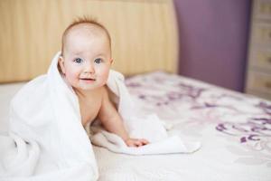 lindo bebê sorridente olhando para a câmera sob uma toalha branca. retrato de uma criança fofa foto