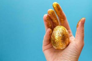ovo de páscoa dourado na mão sobre um fundo azul. fundo de páscoa. mão e ovo em brilhos de ouro. Feliz Páscoa foto