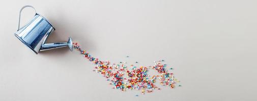 regador prateado derramando açúcar assando granulado colorido em forma de círculo sobre fundo bege claro. bandeira foto