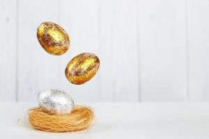 levitação de ovos de páscoa de ouro e prata para o ninho em um fundo claro de madeira. conceito de páscoa. copie o espaço foto