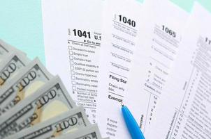 formulários de imposto fica perto de notas de cem dólares e caneta azul sobre um fundo azul claro. restituição do Imposto de Renda foto
