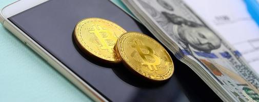 bitcoins encontra-se com os formulários de imposto, notas de cem dólares e smartphone em um fundo azul claro. restituição do Imposto de Renda foto