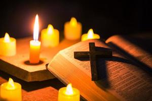 luz de vela com a bíblia sagrada e cruz ou crucifixo sobre fundo de madeira velho na igreja. luz de velas e livro aberto no estudo de cristianismo de mesa de madeira vintage e leitura em casa. conceito de religião de cristo foto