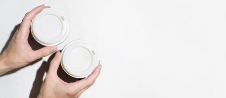 mãos masculinas segurando copos descartáveis com café em um fundo branco, vista superior. bandeira, copie o espaço. conceito de entrega de comida, café para viagem foto