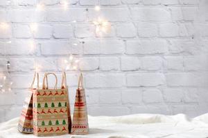 sacos de compras de papel de presentes de natal fundo de parede de tijolo branco e luz de guirlanda foto