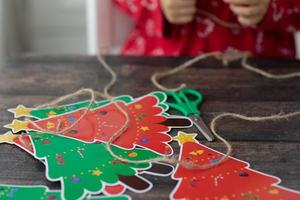 criança faz árvore de natal garaland de papel artesanal de natal na mesa de madeira. mãos de criança. foto