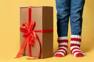 entrega de presentes de natal caixa de papel artesanal e presentes de fita de presente e criança em meias de malha isolado fundo amarelo foto