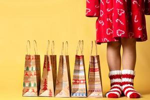 entrega de presentes de natal, sacolas de papel artesanal, presentes e criança em meias de malha, fundo amarelo isolado foto