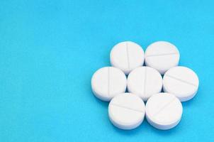 alguns comprimidos brancos repousam sobre uma superfície de fundo azul brilhante. imagem de fundo em tópicos médicos e farmacêuticos foto