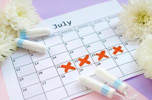 tampões menstruais no calendário do período menstrual com flores brancas em fundo lilás e rosa foto