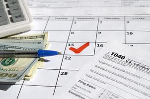 1040 declaração de imposto de renda individual em branco com notas de dólar, calculadora e caneta na página do calendário com 15 de abril marcado foto