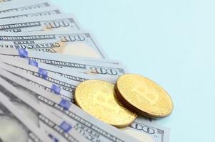 bitcoins dourados e notas de cem dólares estão sobre fundo azul claro foto