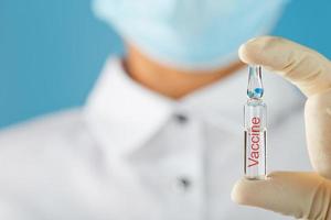 ampola com a vacina contra o vírus de doenças em um fundo azul nas mãos de um médico, cientista em luvas e máscara. foto