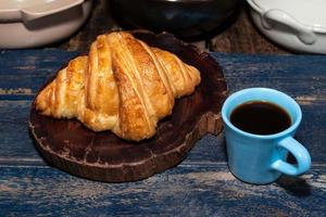 croissant de café da manhã no prato e café na mesa de madeira. foto