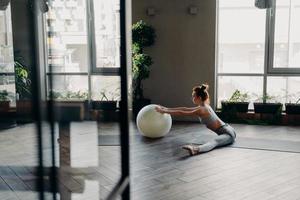 mulher esportiva esticando as pernas em posição dividida, treinando com grande bola de exercício foto