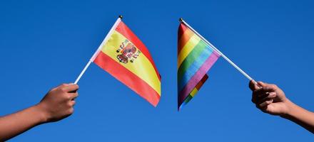 bandeira da espanha e bandeira do arco-íris, símbolo lgbt, segurando nas mãos, fundo azul, conceito para celebração lgbt na espanha e ao redor do mundo no mês do orgulho, junho, foco suave e seletivo, copie o espaço. foto