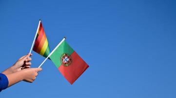 bandeira de portugal e bandeira do arco-íris, símbolo lgbt, segurando nas mãos, fundo azul, conceito para celebração lgbt em portugal e em todo o mundo no mês do orgulho, junho, foco suave e seletivo. foto