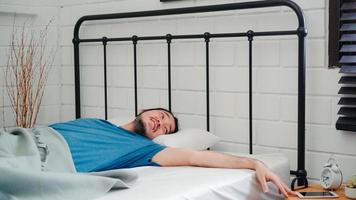 jovem asiático acorda de manhã, homem asiático desliga o despertador no celular depois de acordar na cama no quarto em casa. homens bonitos cochilam, relaxam com sono no conceito de casa moderna. foto