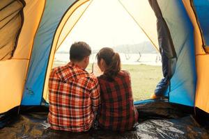 tenda casal despreocupado relaxante conceito de viagem remota - casal de jovens mochileiros sentados em uma tenda olhando para o livro e planejando sua próxima aventura de acampamento foto