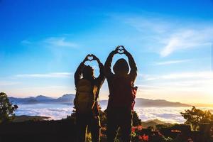 amantes, mulheres e homens asiáticos viajam relaxam no feriado. levantar-se para o nascer do sol na montanha, feliz lua de mel, levantou a mão para fazer um formato de coração. foto