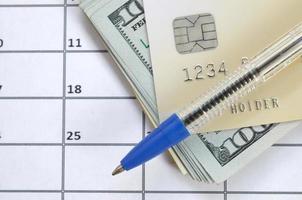 caneta e cartão de crédito em muitas centenas de notas de dólar americano na página do calendário close-up foto