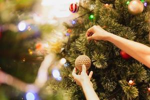 a mão de uma mulher pendura uma bola de natal na árvore de natal feriado festivo. foto