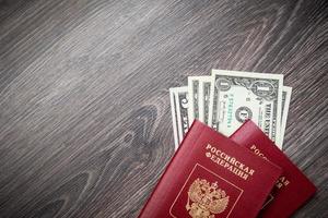um passaporte estrangeiro e dólares em um fundo de madeira. foto