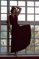 mulher em um vestido vermelho com a perna dobrada na frente da janela foto