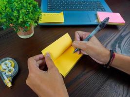 as mulheres escrevem em notas amarelas, simulam notas amarelas. as mãos das mulheres escrevem notas em papel de nota amarelo no fundo do espaço de trabalho da mesa de escritório da vista superior. foto