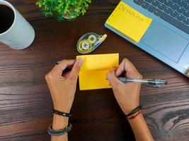 as mulheres escrevem em notas amarelas, simulam notas amarelas. as mãos das mulheres escrevem notas em papel de nota amarelo no fundo do espaço de trabalho da mesa de escritório da vista superior. foto