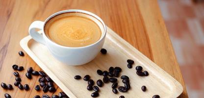 xícara branca de café expresso e grãos de café torrados no balcão de madeira na cafeteria foto