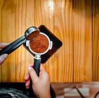 barista derrama café torrado em pó café moído despejando em um porta-filtro com uma mão de barista na cafeteria foto