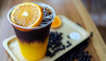 menu de bebida de café gelado laranja americano com frutas frescas de laranja misturadas em um copo de plástico no balcão de madeira do café foto