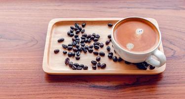 xícara branca de café expresso e grãos de café torrados em uma bandeja de madeira foto