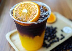menu de bebida de café gelado laranja americano com frutas frescas de laranja misturadas em um copo de plástico no balcão de madeira do café foto