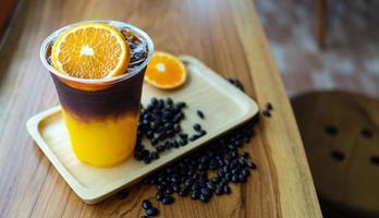 menu de bebida de café gelado laranja americano com frutas frescas de laranja misturadas em um copo de plástico no balcão de madeira do café foto