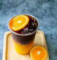 menu de bebida de café gelado laranja americano fusão com frutas frescas de laranja misturadas em um copo de plástico, produto do menu de bebidas. foto